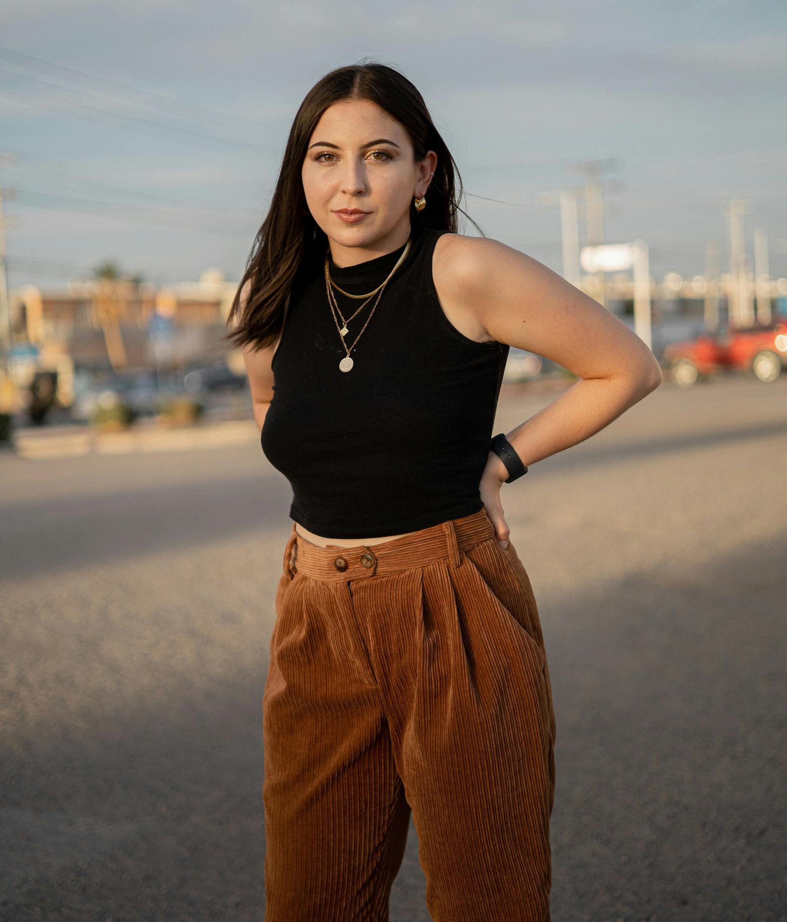 Woman in black crop top and brown pants posing outdoors at sunset.